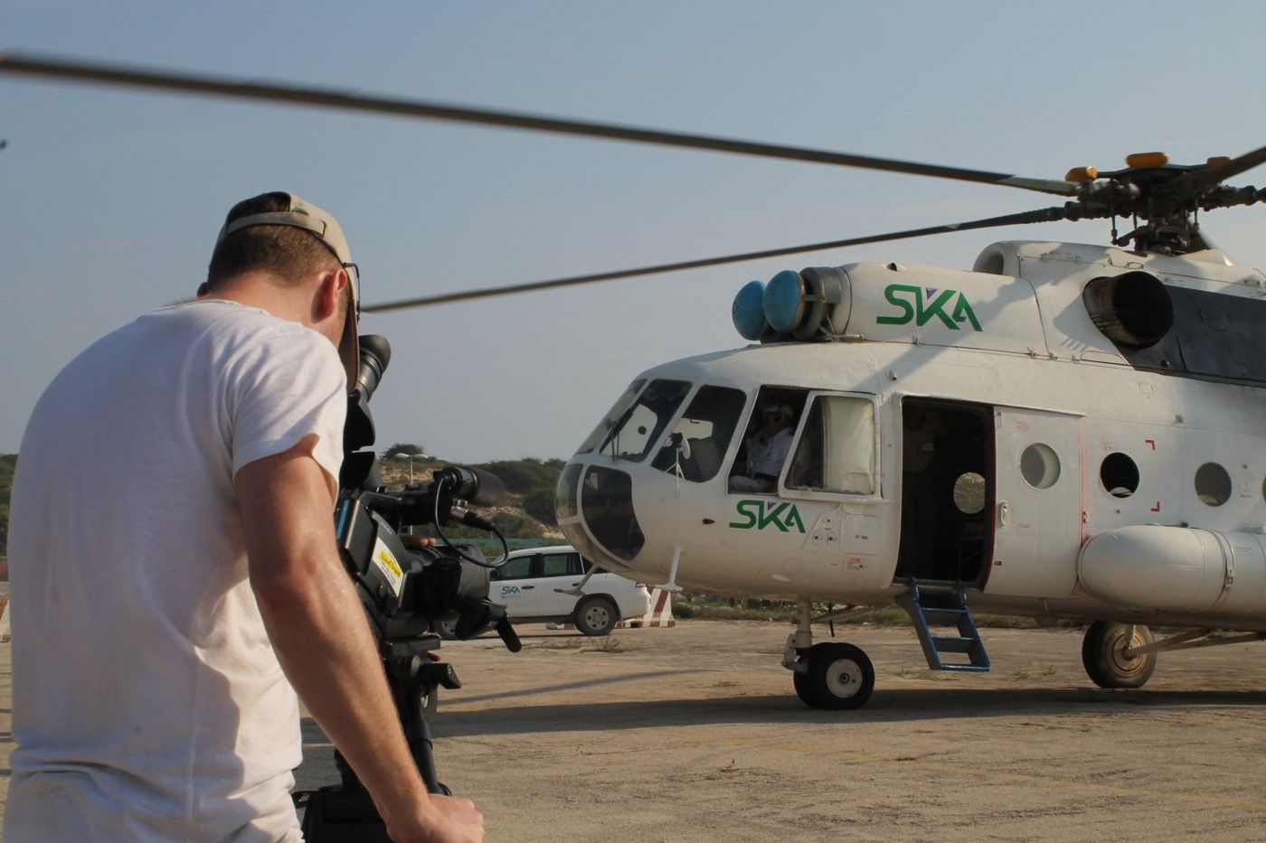 Camera operator filming beside a helicopter on an airfield