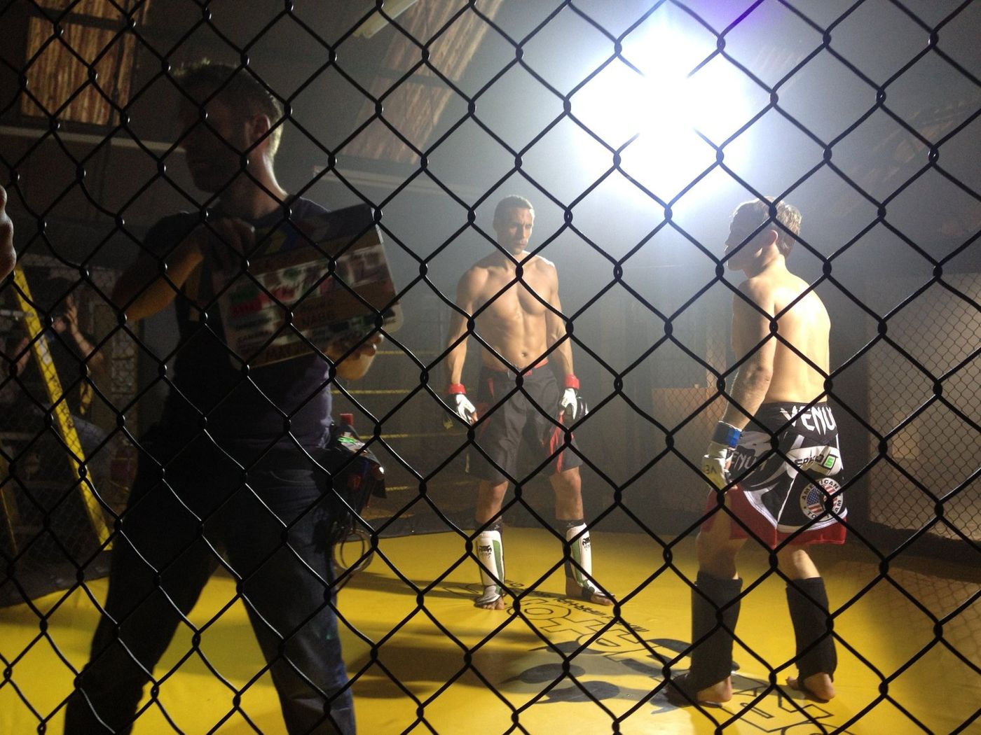Camera operator filming two fighters inside a cage